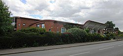 ![A red brick building on a street with trees in the background.